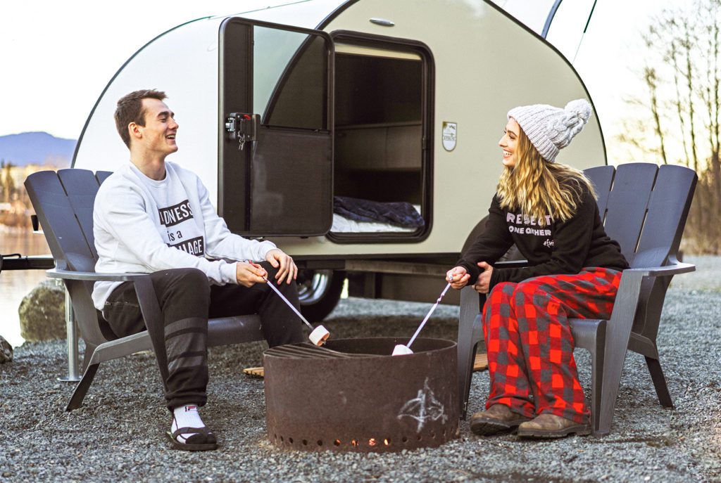 Man and woman camping and sitting outside roasting marshmallows by their Evolve Solar Teardrop Trailer